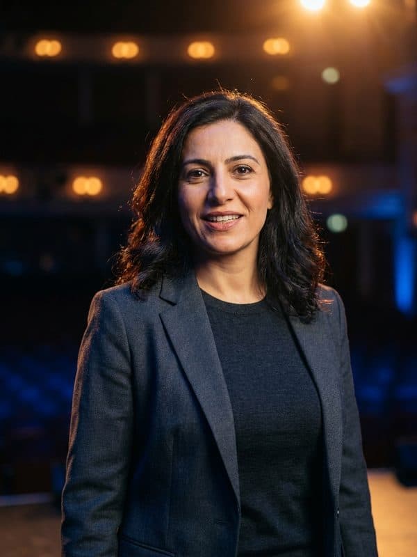 AI-generated example of a Conference Speaker headshot: warm stage light with blurred audience lights behind